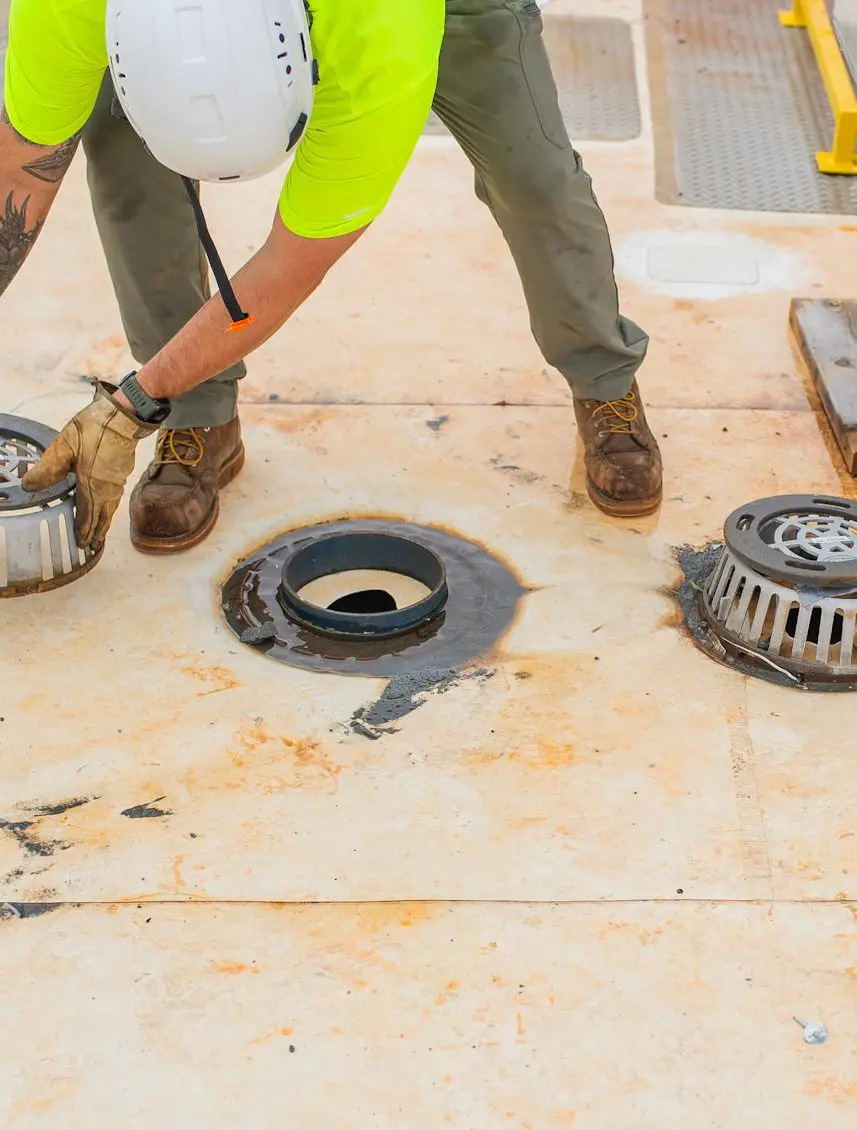 Worker clearing commercial roof drain during maintenance service
