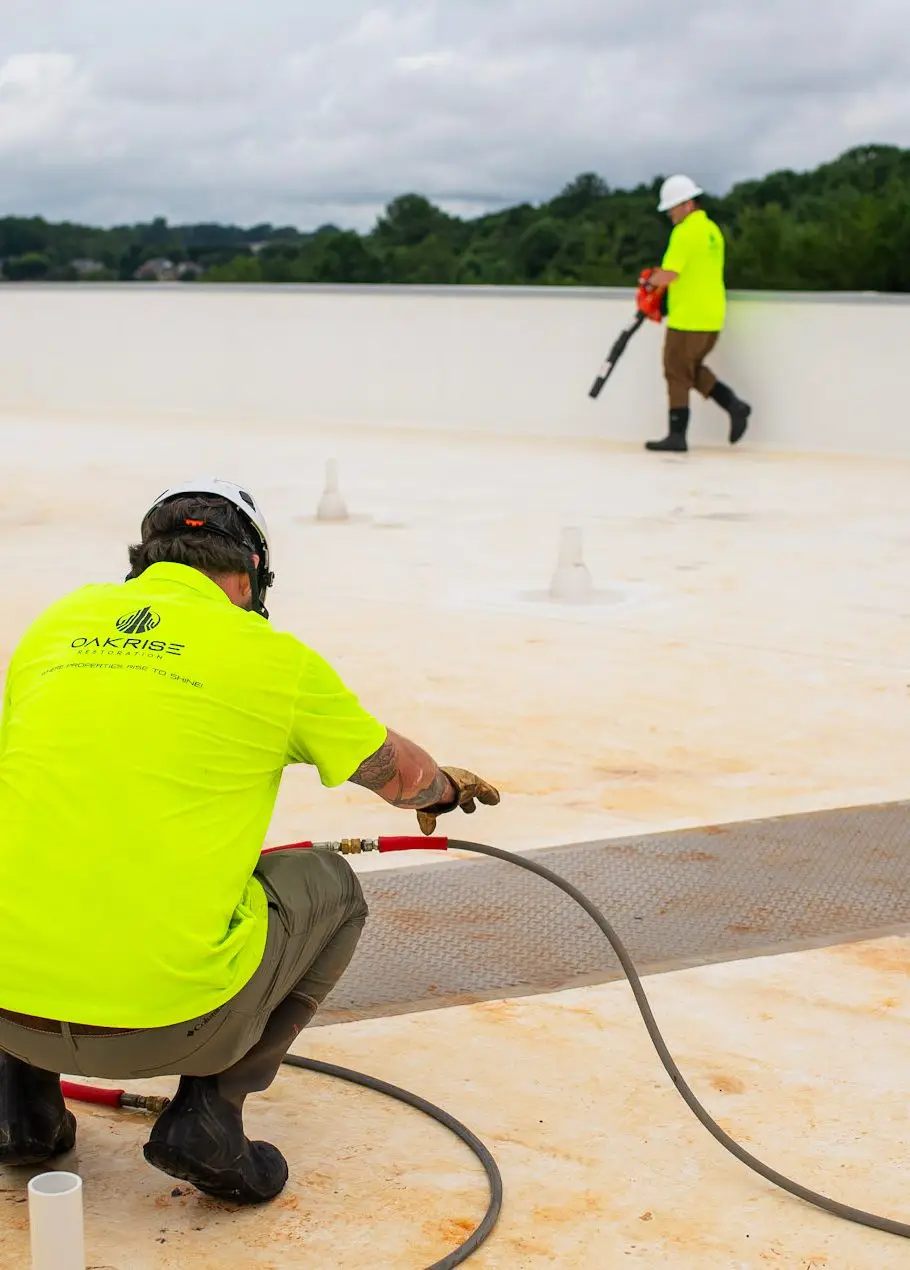 Technician soft washing commercial flat roof with controlled low-pressure system